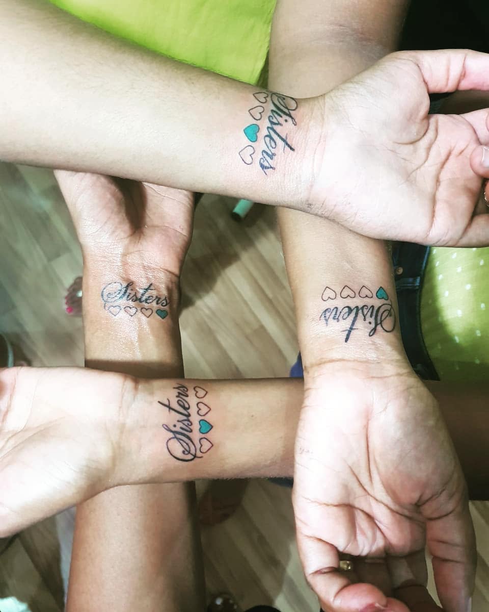 Four hands with matching "Sisters" tattoos and heart designs on their wrists